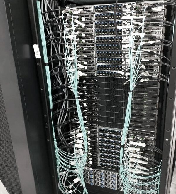 High-density fibre patching on a GPU cluster switch — colour-sorted aqua jumpers, each labelled
